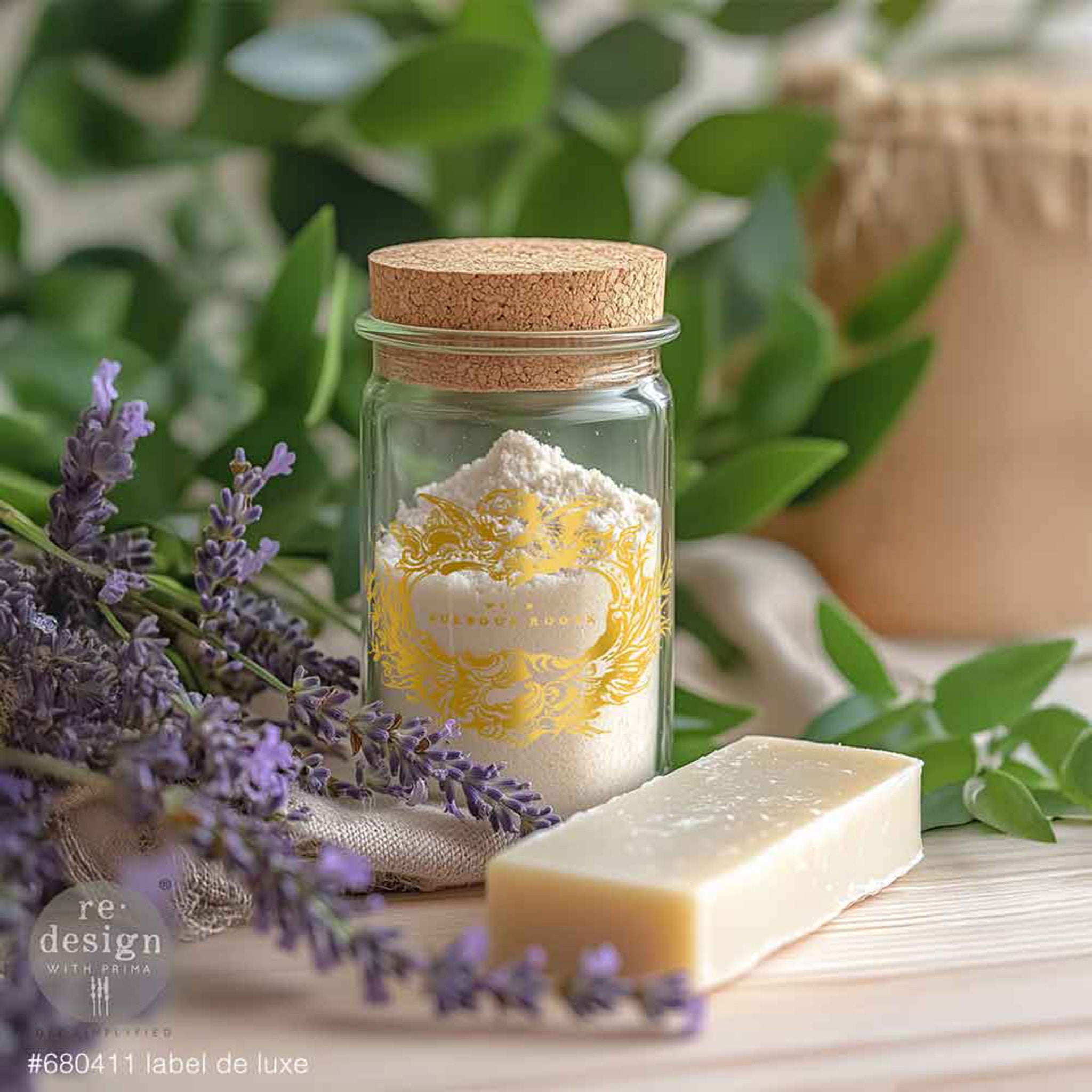 Jar of bath salts with a cork lid, bar of soap, and lavender flowers on a wooden surface with greenery in the background.