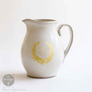 White ceramic pitcher with gold decorative elements on a white background, featuring the Redesign with Prima logo.