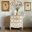 A vintage 3-drawer night stand is painted cream and features ReDesign with Prima's Queen's Glory small rub-on transfers on the drawers.