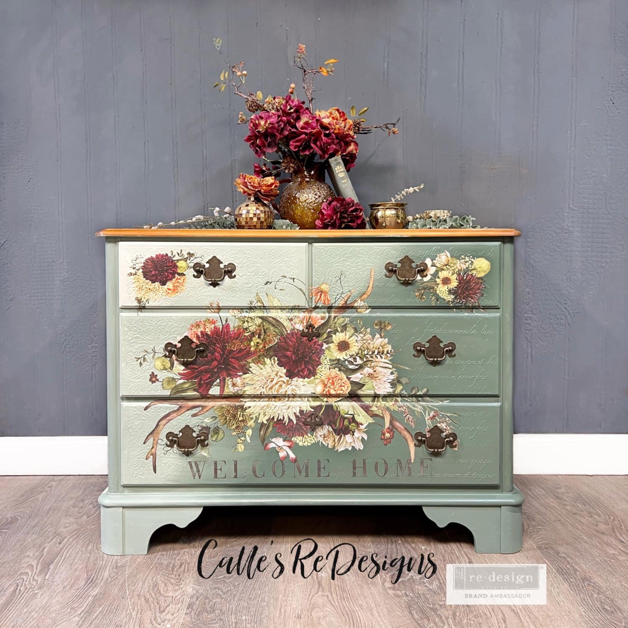 A 4 drawer dresser refurbished by Calle's ReDesigns is painted an ombre of light and sage green and features ReDesign with Prima's Rustic Charm furniture transfer on the front.