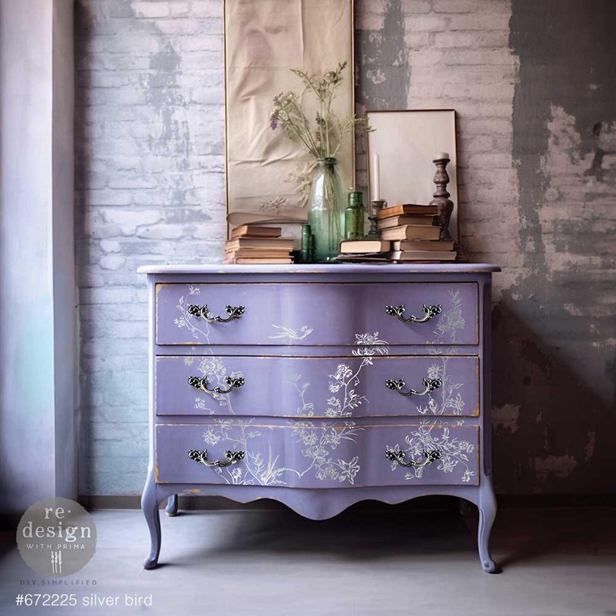 A vintage 3-drawer dresser is painted lavender purple and features ReDesign with Prima's Kacha Silver Bird Silver Foil transfer on the front.