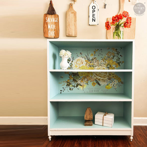A small 3 shelf bookcase is painted sky blue and features ReDesign with Prima's Sunlit Serenade rub-on furniture transfer on the backboard.