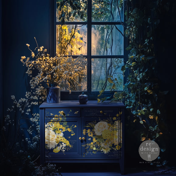 A small buffet table set in a dark blue room with white flowers is painted navy blue and features ReDesign with Prima's Sunlit Serenade rubon furniture transfer on the front.