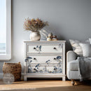 Decorative chest of drawers with nature-themed design in a room with a couch and window.