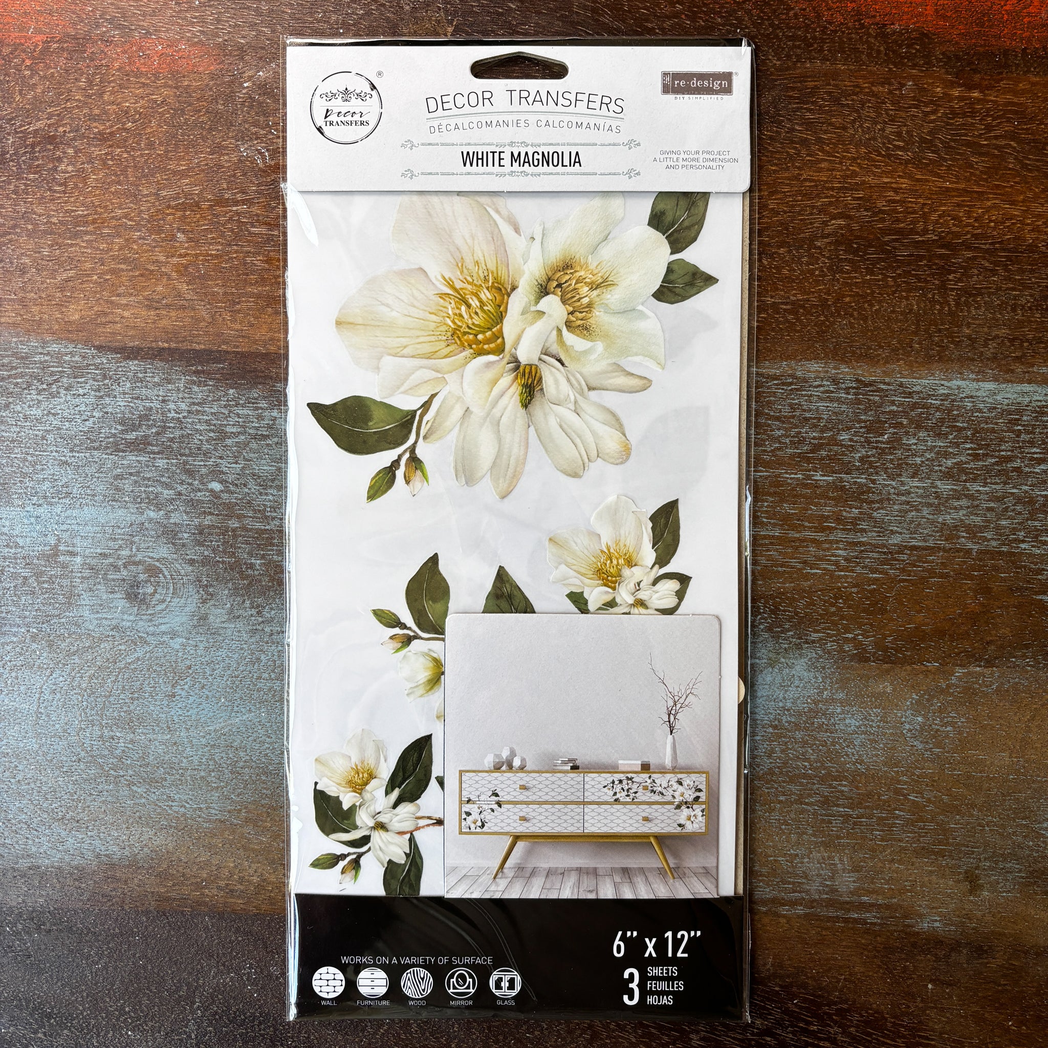 A package of ReDesign with Prima's White Magnolia small transfer is against a dark wood background.