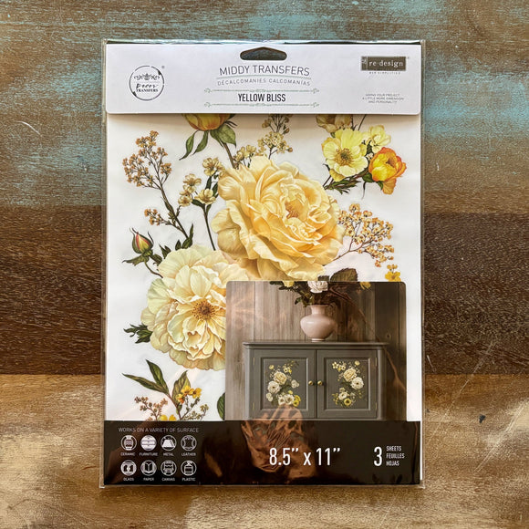 A package of ReDesign with Prima's Yellow Bliss small rub-on transfers is against a wood background.