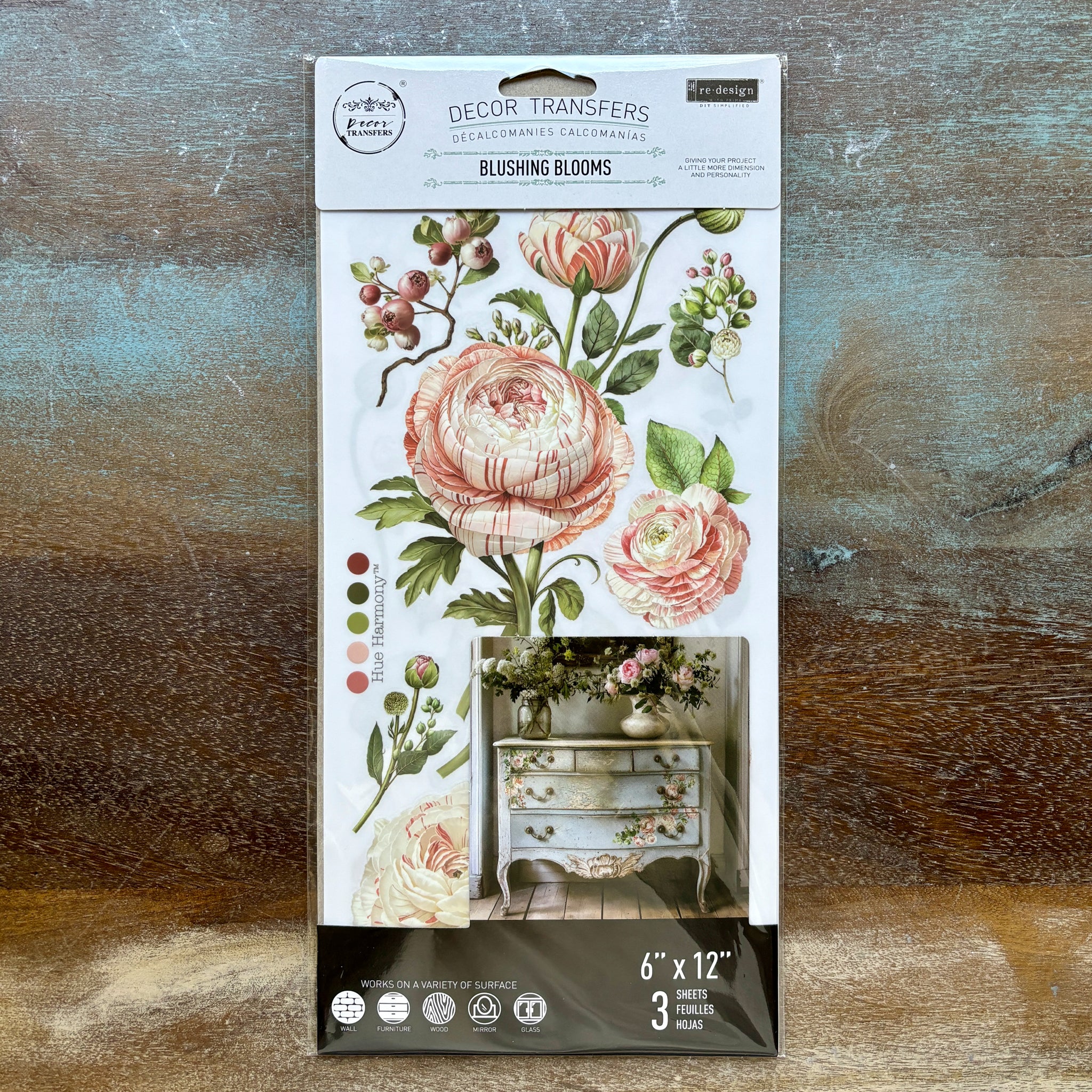 A package of ReDesign with Prima's Blushing Blooms small rub-on transfers is against a wood background.