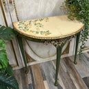 Decorative half-moon table with floral design and gold accents on a wooden floor.