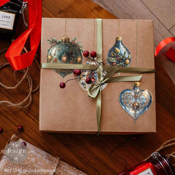 A brown square box with a gold ribbon features glass ornament designs from ReDesign with Prima's Gilded Elegance middy rub-on transfers on the lid.