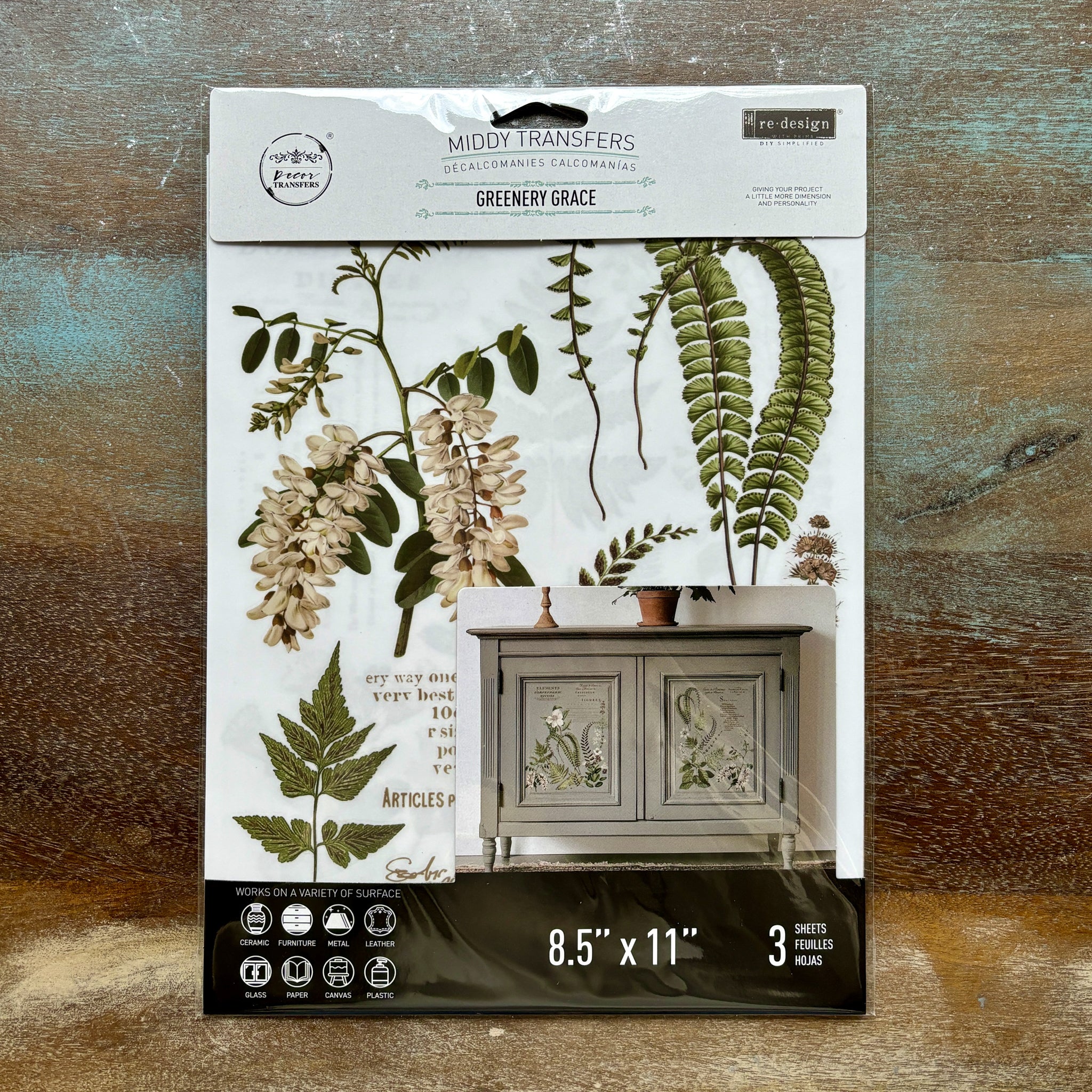 A package of ReDesign with Prima's Greenery Grace small rub-on transfers is against a wood background.