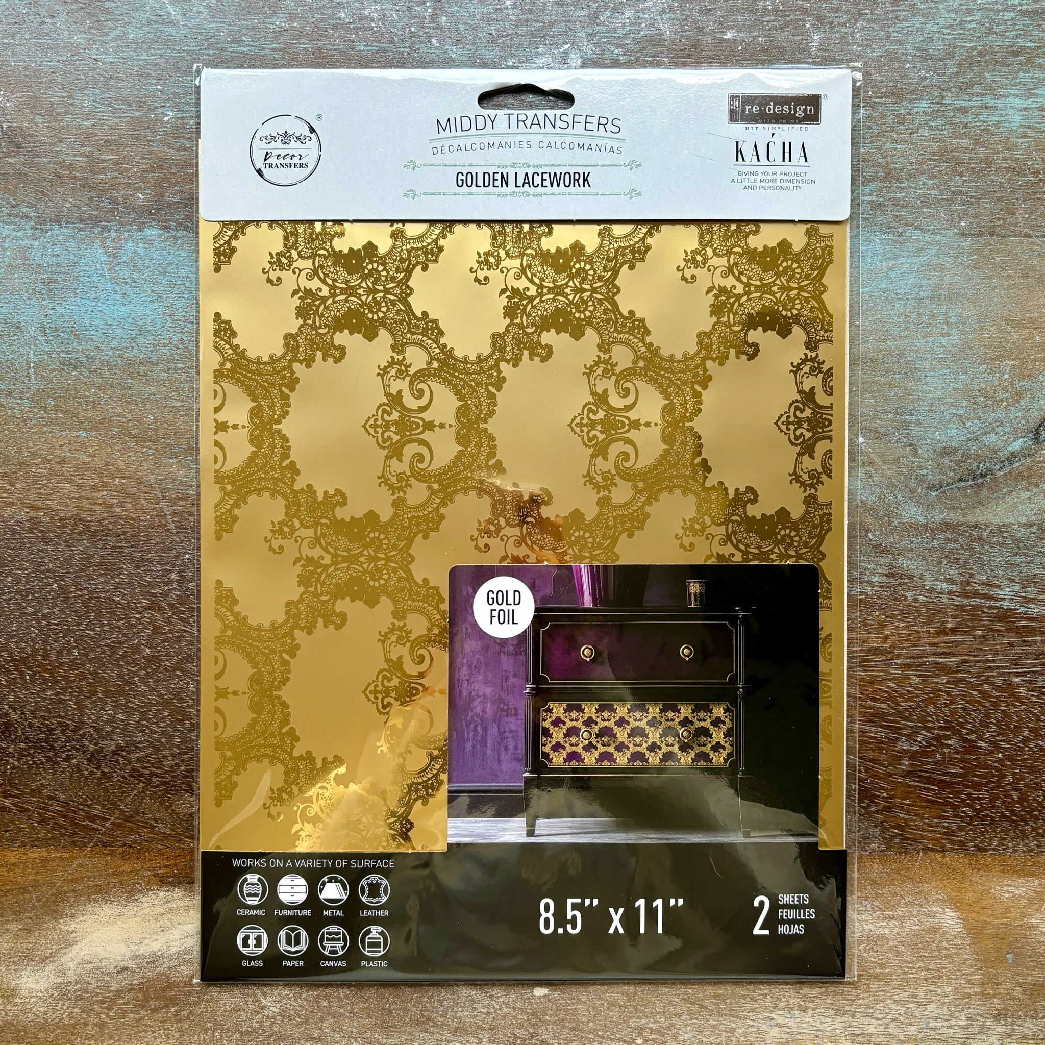 A package of ReDesign with Prima's Golden Lacework gold foil small rub-on transfers is against a wood background.