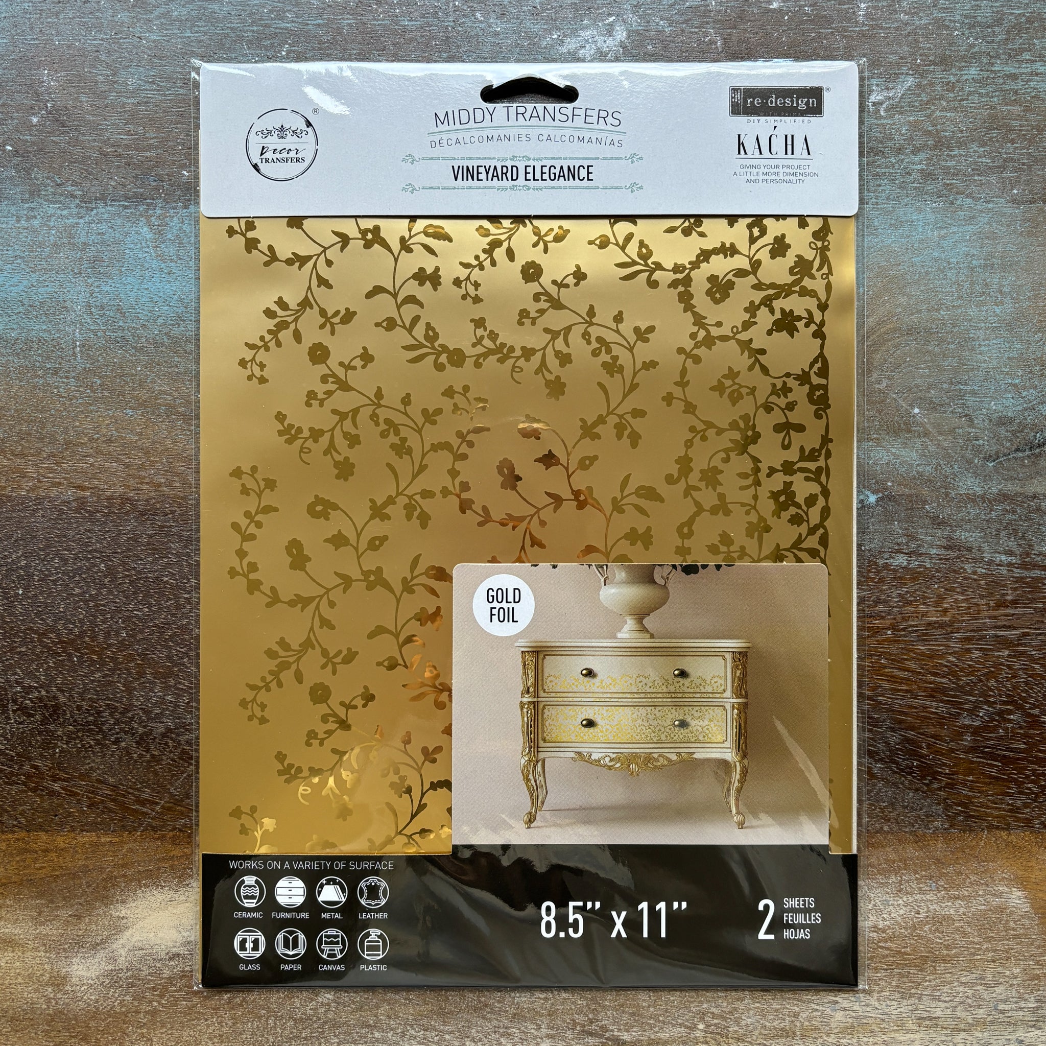 A package of ReDesign with Prima's Kacha Vineyard Elegance gold foil small rub-on transfers is against a wood background.