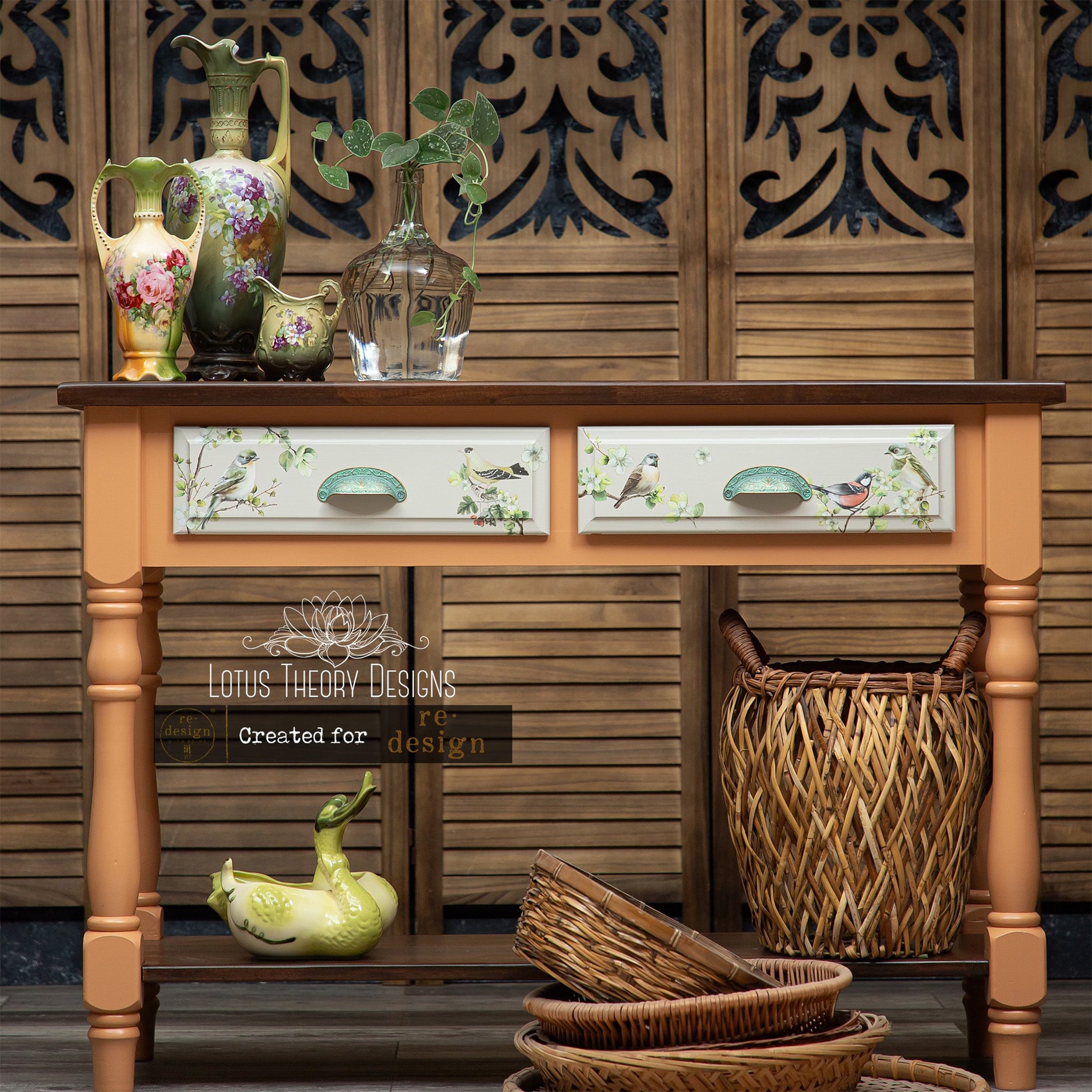 A vintage console table with 2-drawer storage refurbished by Lotus Theory Designs is painted pale orange with white drawers and features ReDesign with Prima's Nestled Whispers rub-on transfer on the drawers.