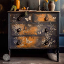 A vintage 4-drawer dresser is painted black with patches of orange and features ReDesign with Prima's Quiet Contemplation middy rub-on transfers on the front.