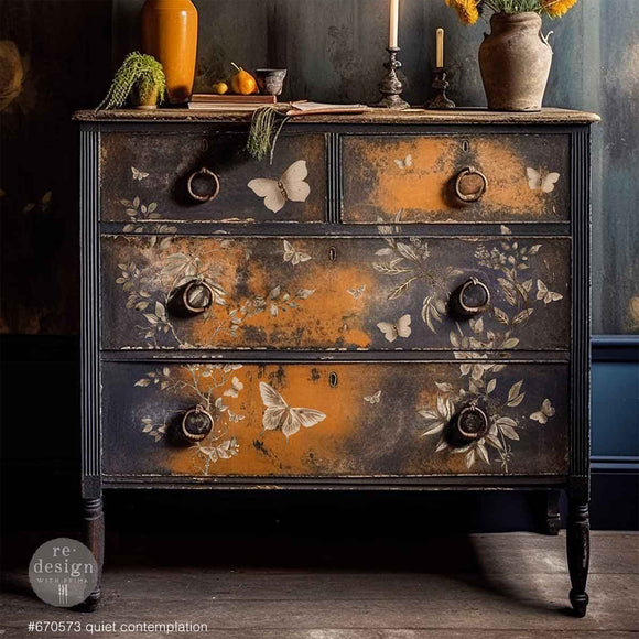 A vintage 4-drawer dresser is painted black with patches of orange and features ReDesign with Prima's Quiet Contemplation middy rub-on transfers on the front.