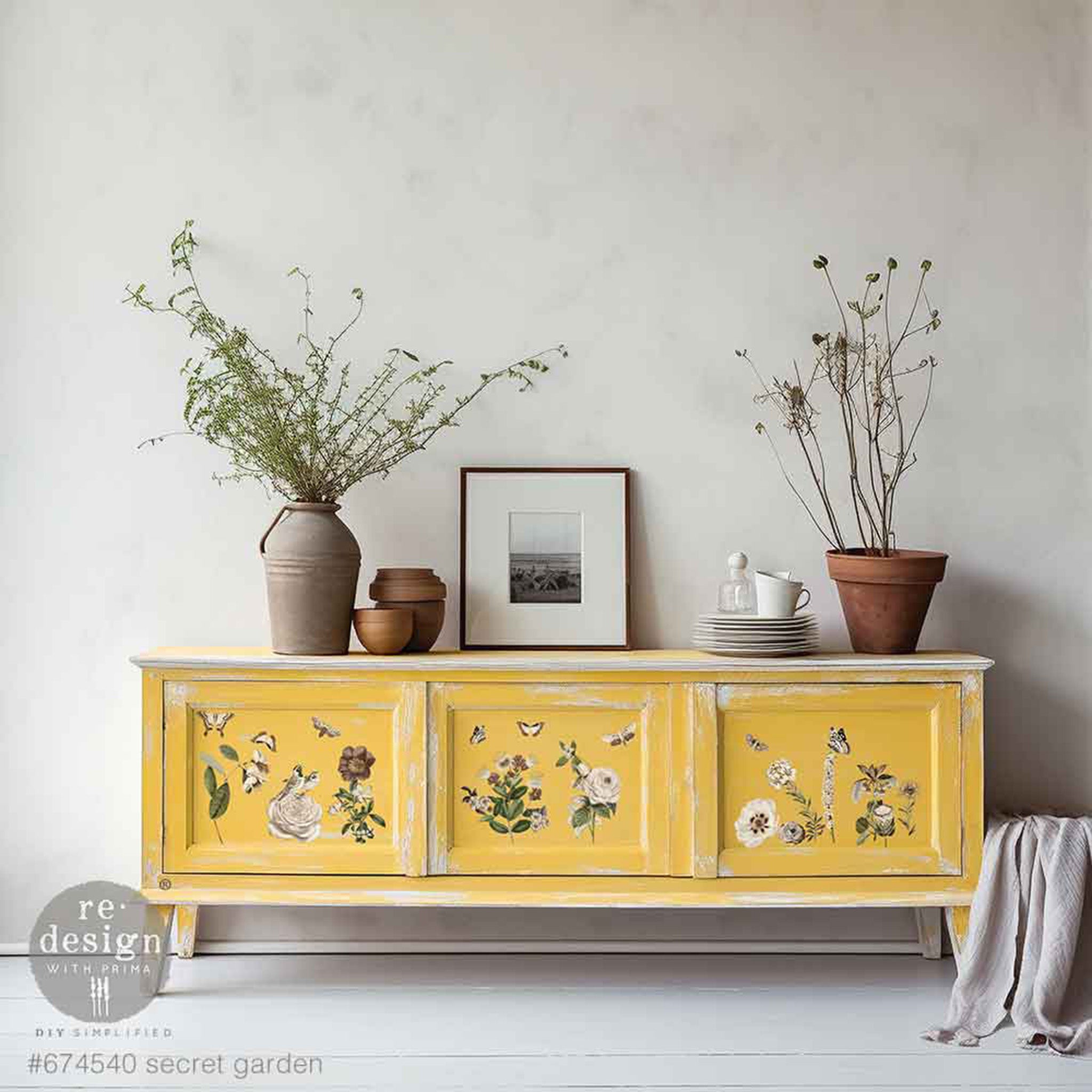 A vintage console table with 3 doors is painted soft sunshine yellow and features ReDesign with Prima's Secret Garden small rub-on transfers on its doors.