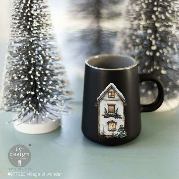 A black coffee mug next to a small craft Christmas tree features a design from ReDesign with Prima's Village of Wonder middy rub-on transfers.