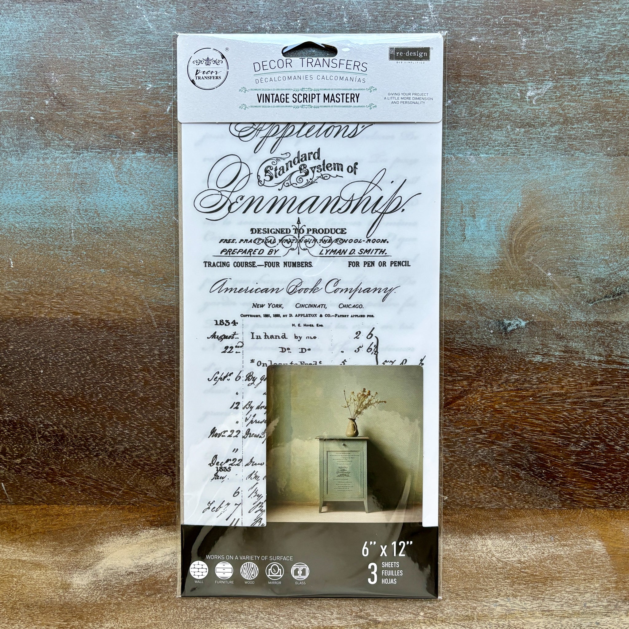 A package of ReDesign with Prima's Vintage Script Mastery small rub-on transfers is against a wood background.