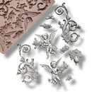 A silicone mold and silver colored castings featuring cherubs, intricate scrolling designs, and a vase with roses around it are against a white background.