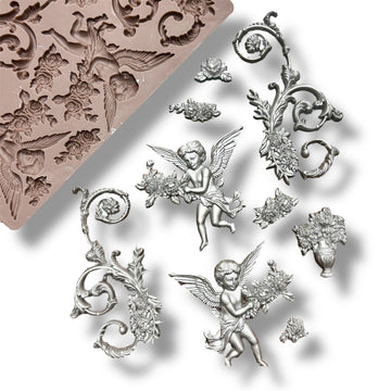 A silicone mold and silver colored castings featuring cherubs, intricate scrolling designs, and a vase with roses around it are against a white background.