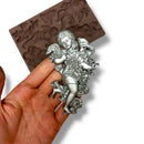 Silver angel figurine held by a hand with a silicone mold in the background
