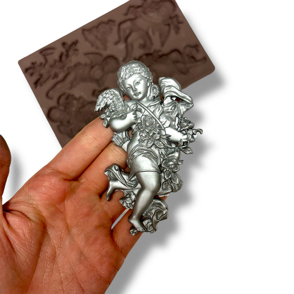 Silver angel figurine held by a hand with a silicone mold in the background
