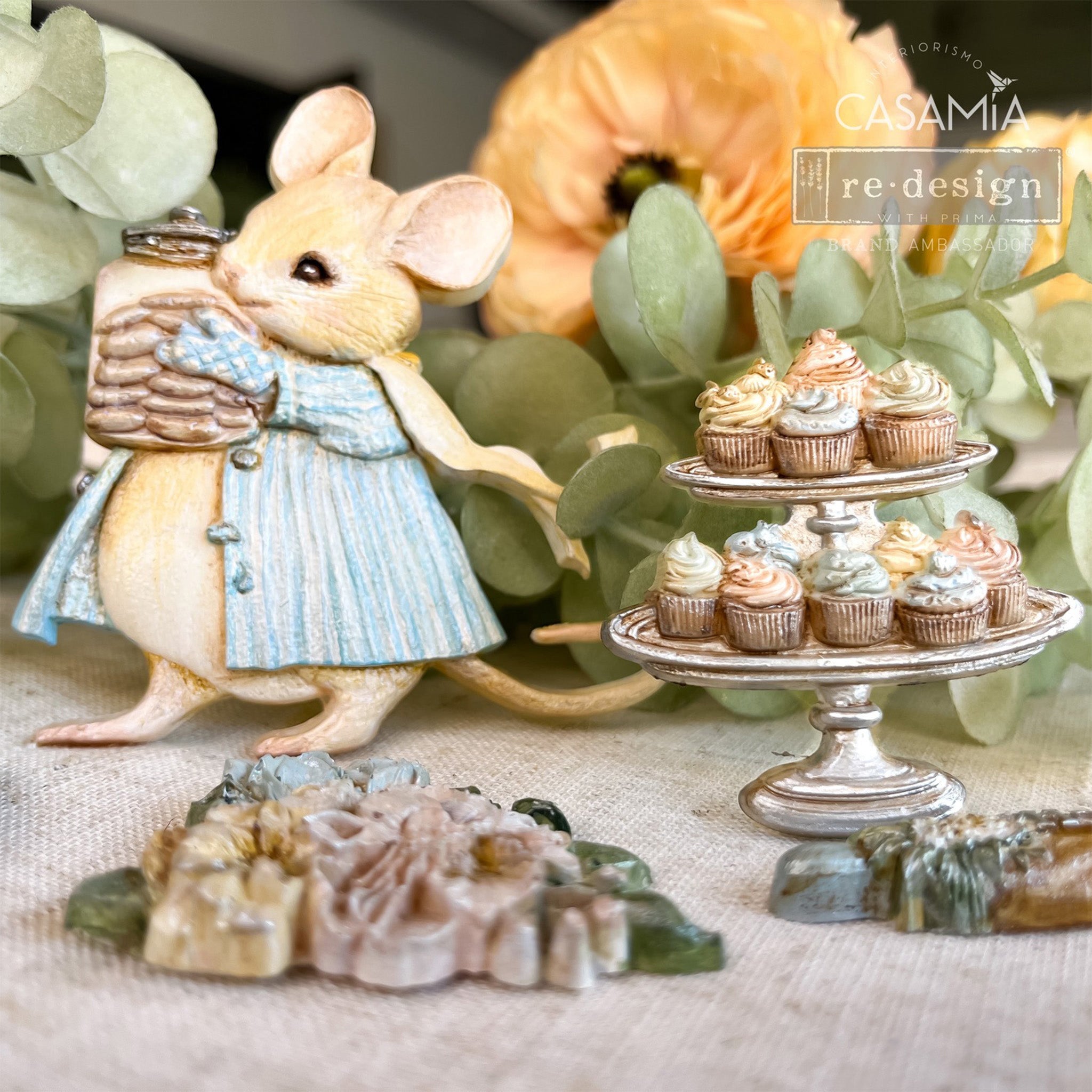 Close-ups of colorful castings created by Casamia that were made from Prima Marketing's Bakers Delight silicone mold are set up in front of some light green plants and an orange flower.