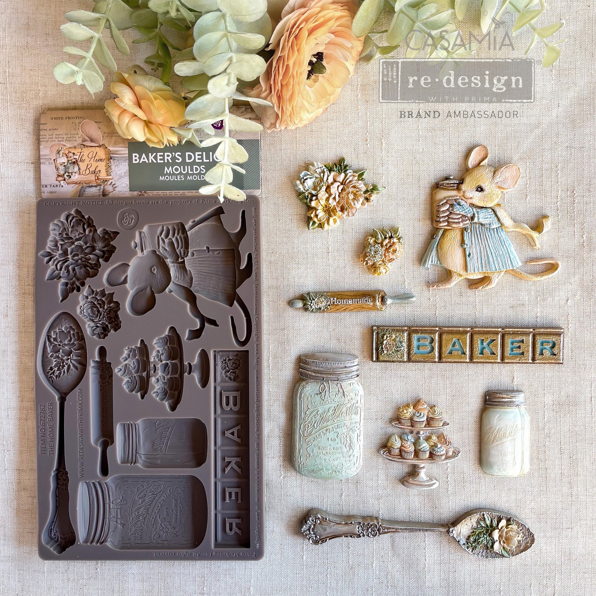 A brown silicone mold and colorful castings of 2 small floral bouquets, a little baker mouse and other baking needs like a spoon, rolling pin, mason jars, and a 2-tier cupcake tray are against a linen background.