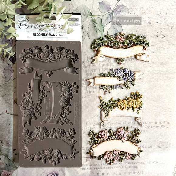 A package and colorful castings of ReDesign with Prima's Blooming Banners silicone mold are against a white wood background.