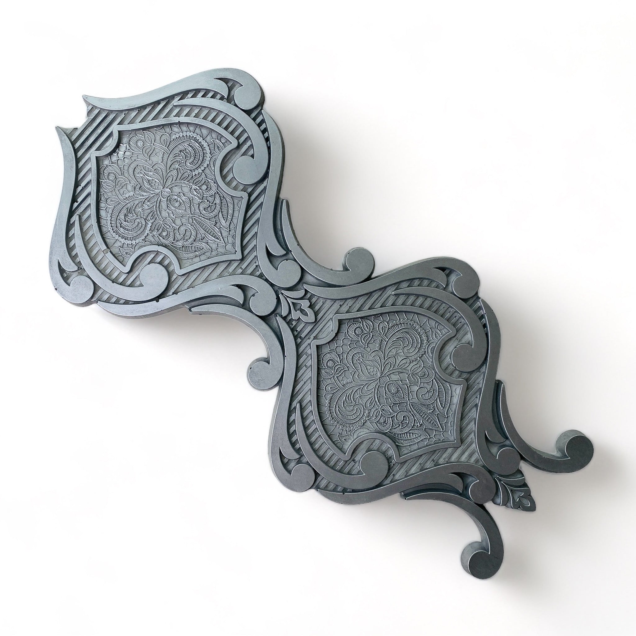 A silver-colored silicone mold casting that features a large hourglass shaped medallion is against a white background.