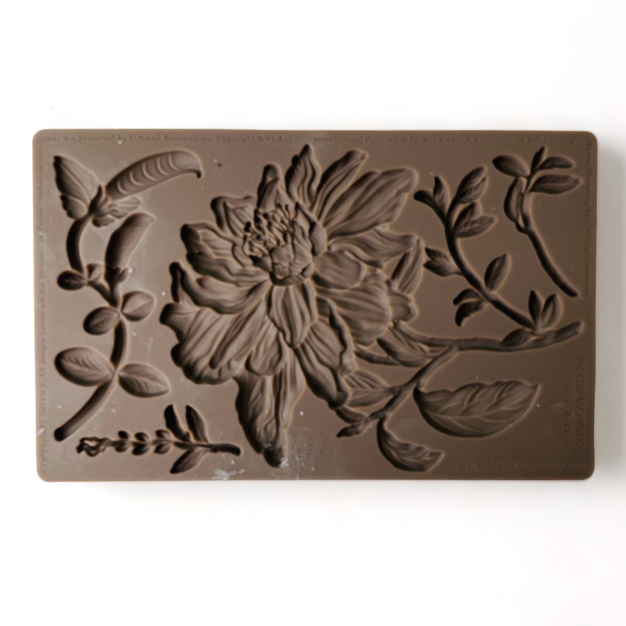 A brown silicone mold of a large flower bloom with foliage is against a white background.