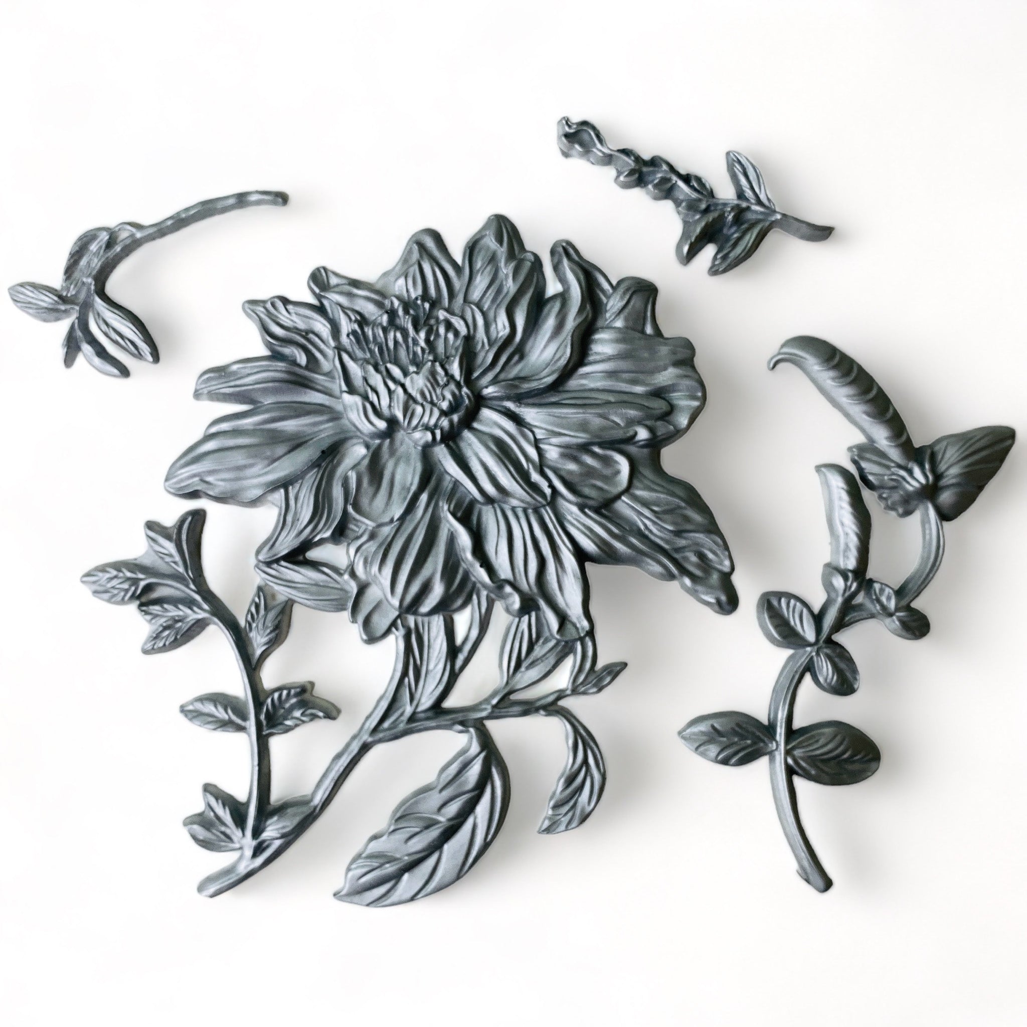 Silver-colored silicone mold castings of a large flower bloom with foliage are against a white background.