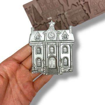 Silver building-shaped object held in a hand with a mold in the background