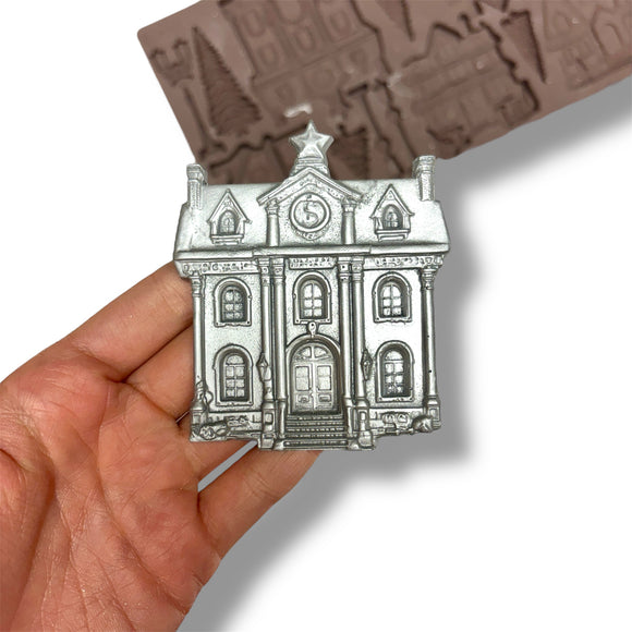 Silver building-shaped object held in a hand with a mold in the background