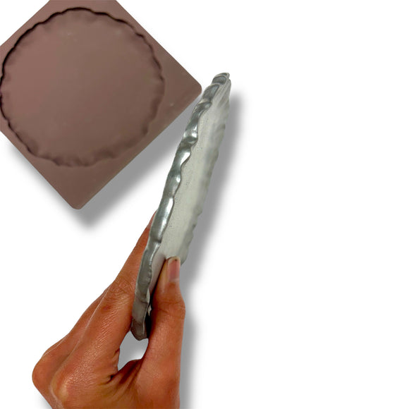 Hand holding a silver plate with a brown silicone mold on a white background