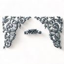 Silver-colored silicone mold castings that feature 2 scrolling vine corners and a small center accent scroll are against a white background.