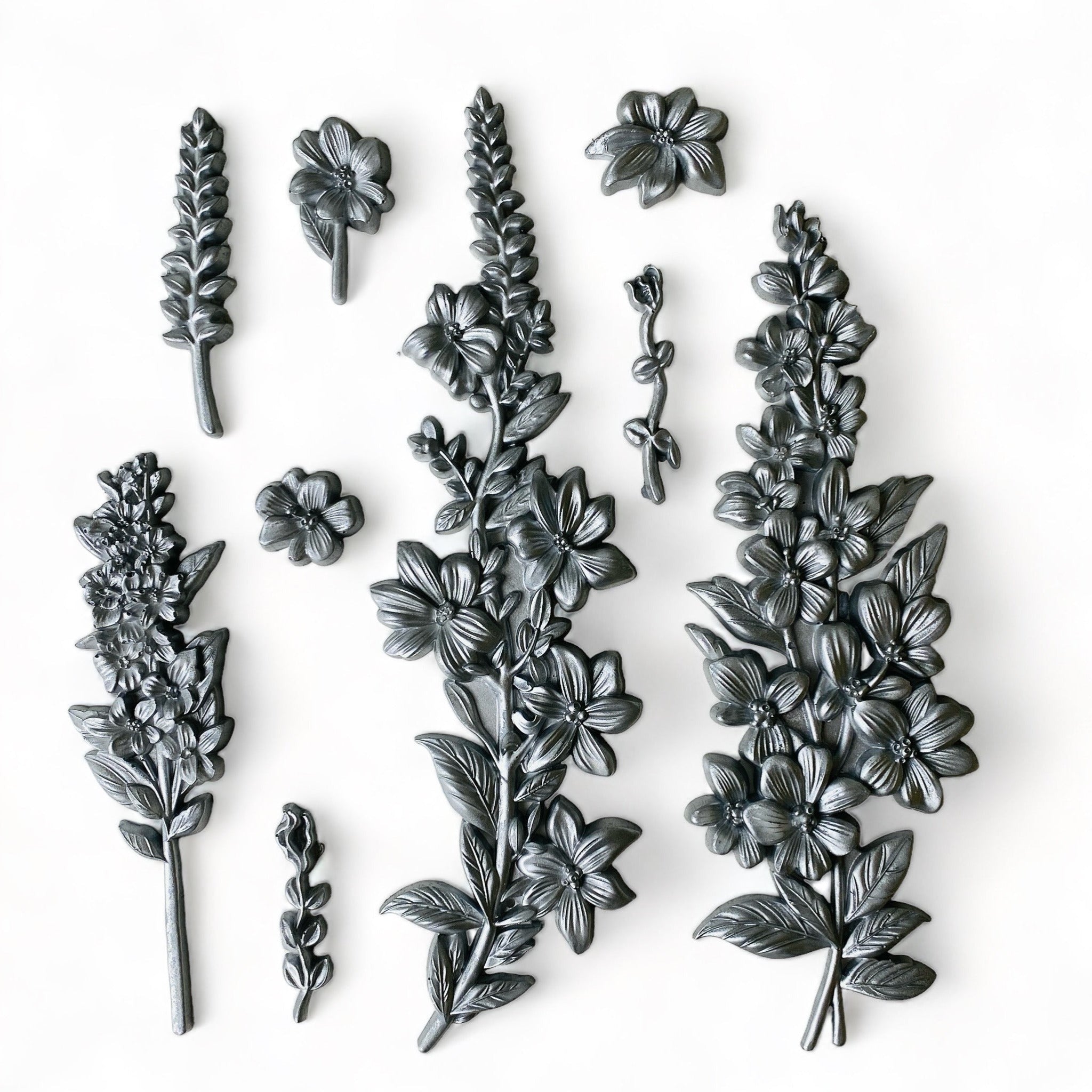 Silver-colored silicone mold castings that feature petite flower clusters are against a white background.