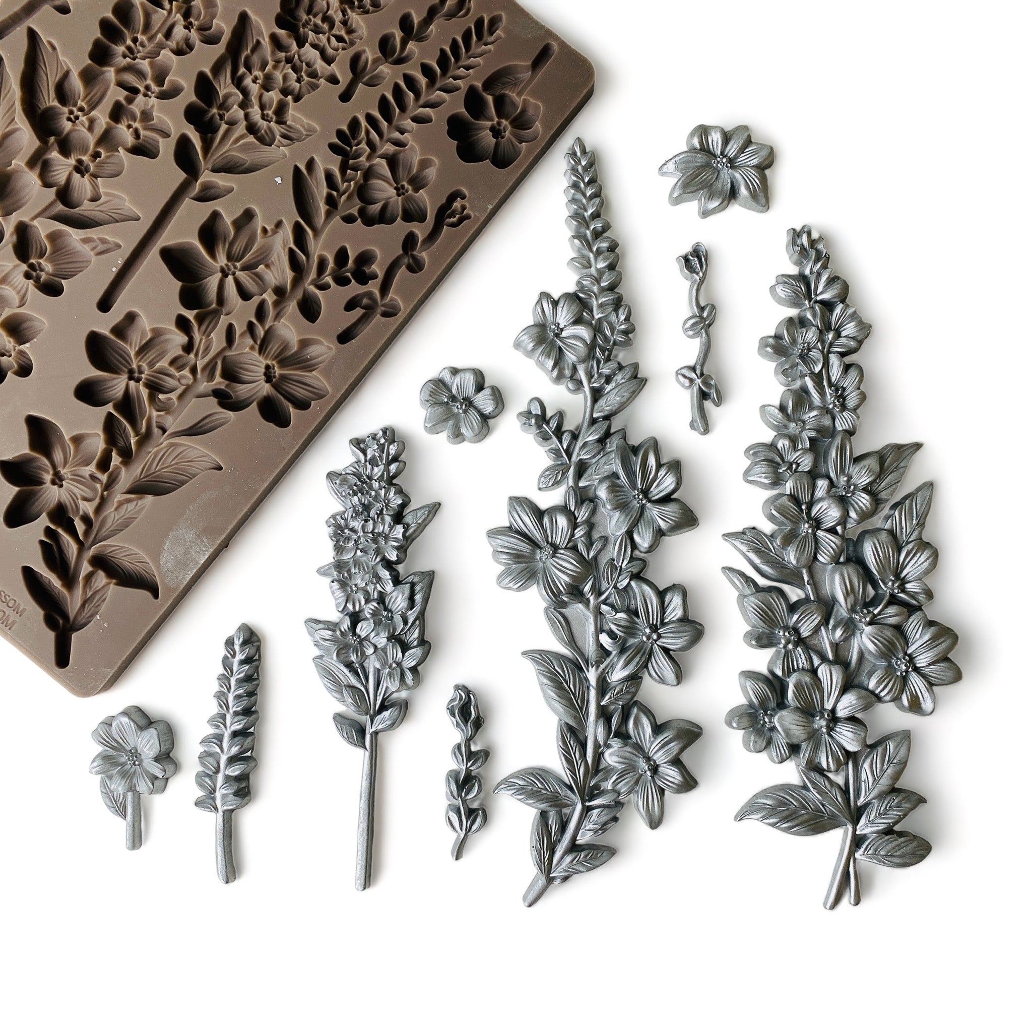 A brown silicone mold and silver-colored castings that feature petite flower clusters are against a white background.