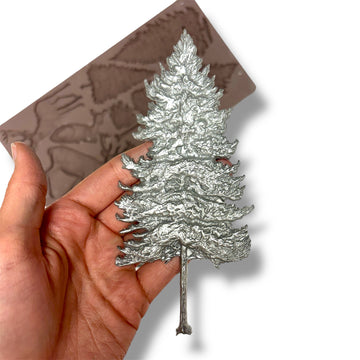 Silver tree-shaped object held in a hand with a brown silicone mold in the background