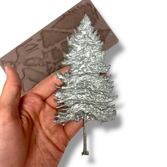 Silver tree-shaped object held in a hand with a brown silicone mold in the background