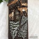 Decorative wall art with deer and pine tree designs on a textured surface.