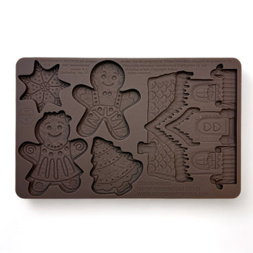 A brown silicone mold featuring gingerbread designs in the shape of a cookie man, cookie woman, Christmas tree, snowflake, and even a gingerbread house is against a white background.