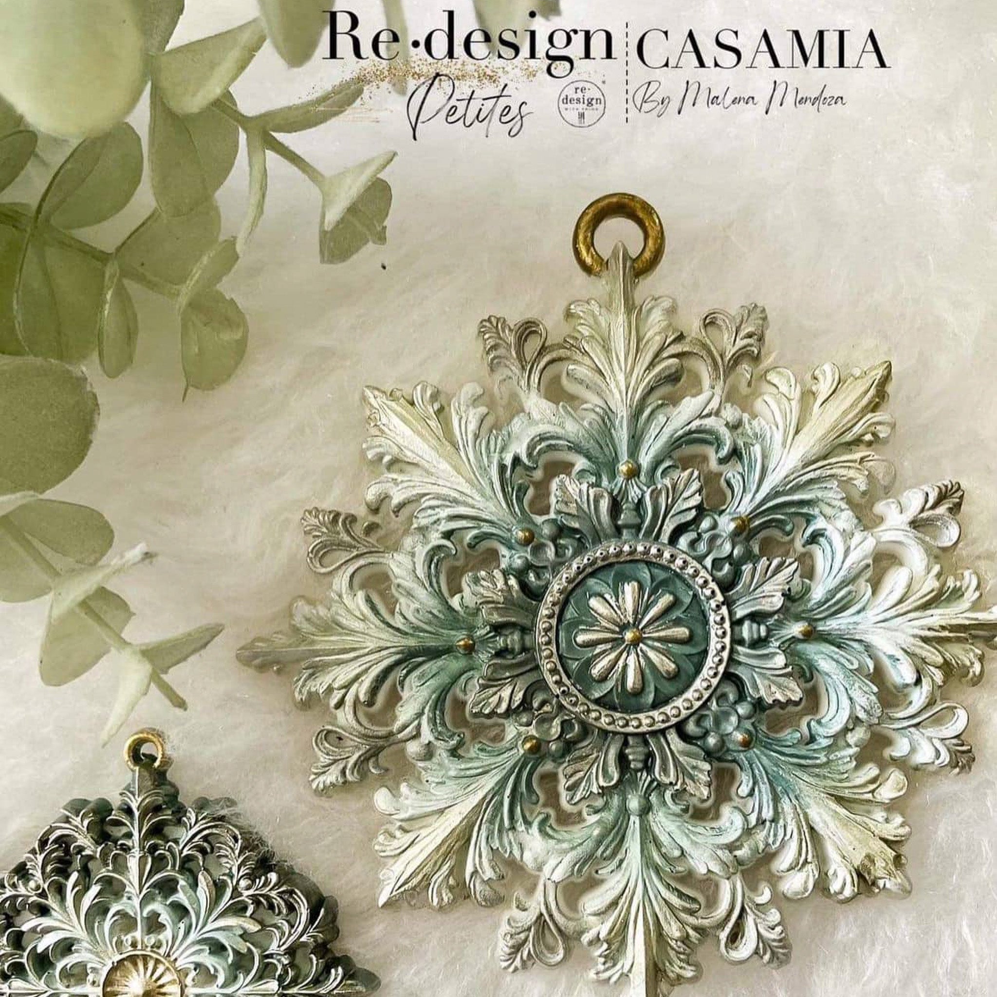 Dark green, white, and gold painted castings created by Casamia by Malena Mendoza of ReDesign with Prima's Frost Spark silicone mould are set against a beige background with green foliage in the top left corner.