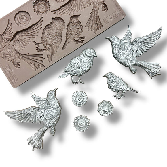 A silicone mold and silver colored castings featuring 4 birds adorned in cogs and gears, along with 3 separate gears are against a white background.