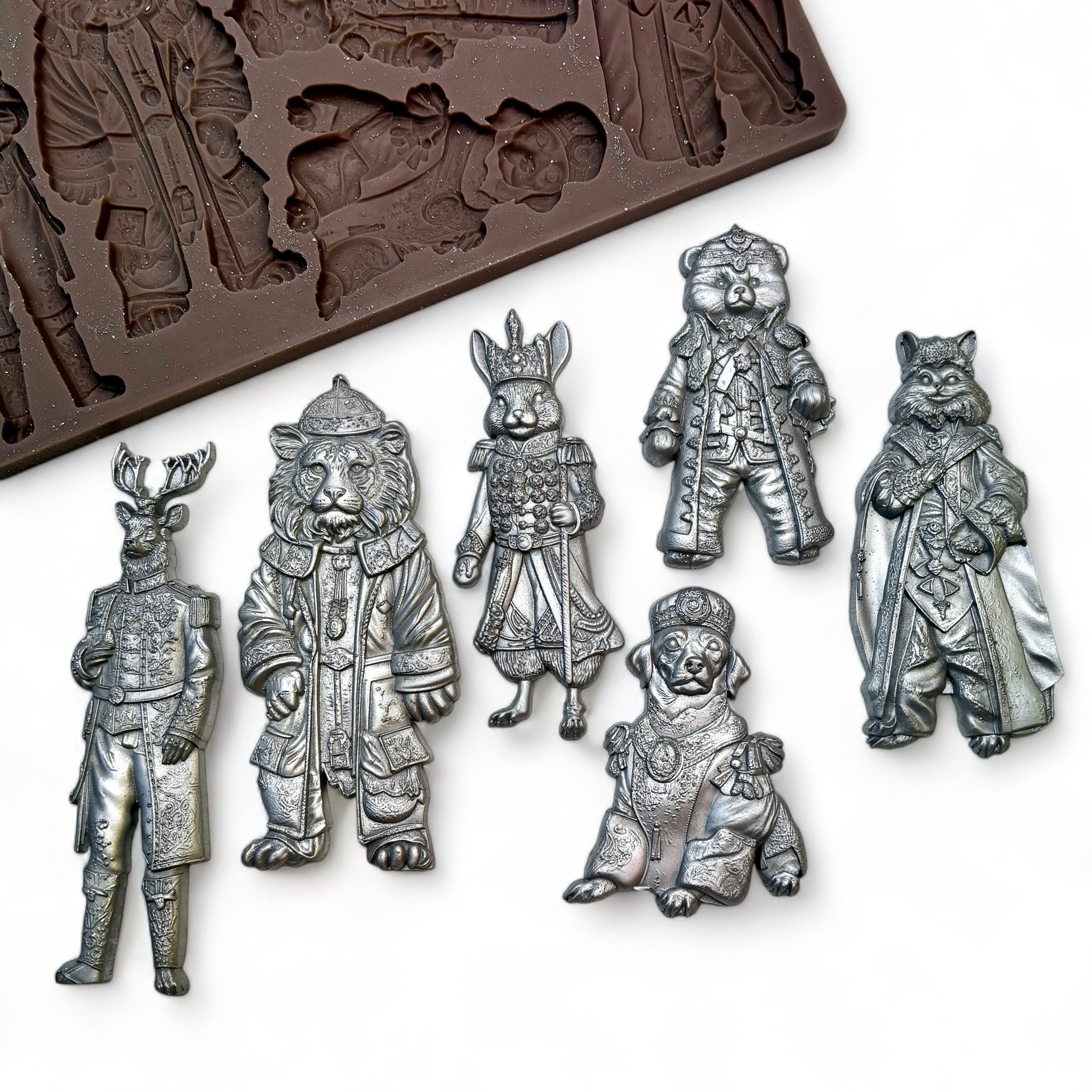 A brown silicone mold and silver colored castings of 6 upright animal characters dressed in winter clothing are against a white background.