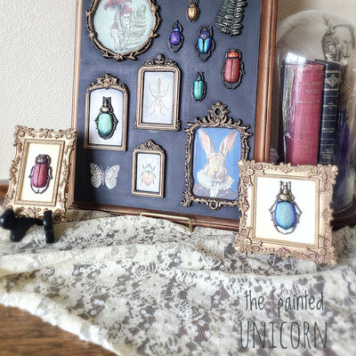 Decorative wall art with framed illustrations and small objects on a textured surface.