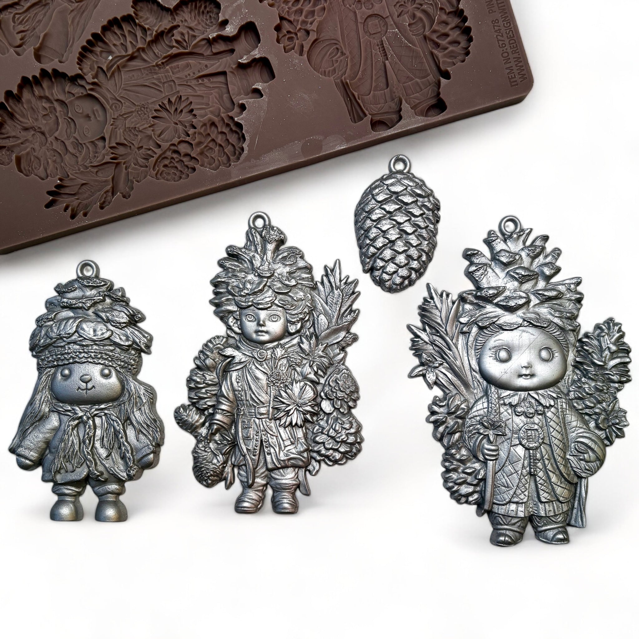 A brown silicone mold and silver colored castings of a small single pinecone and 3 ornaments of pinecone dolls are against a white background.