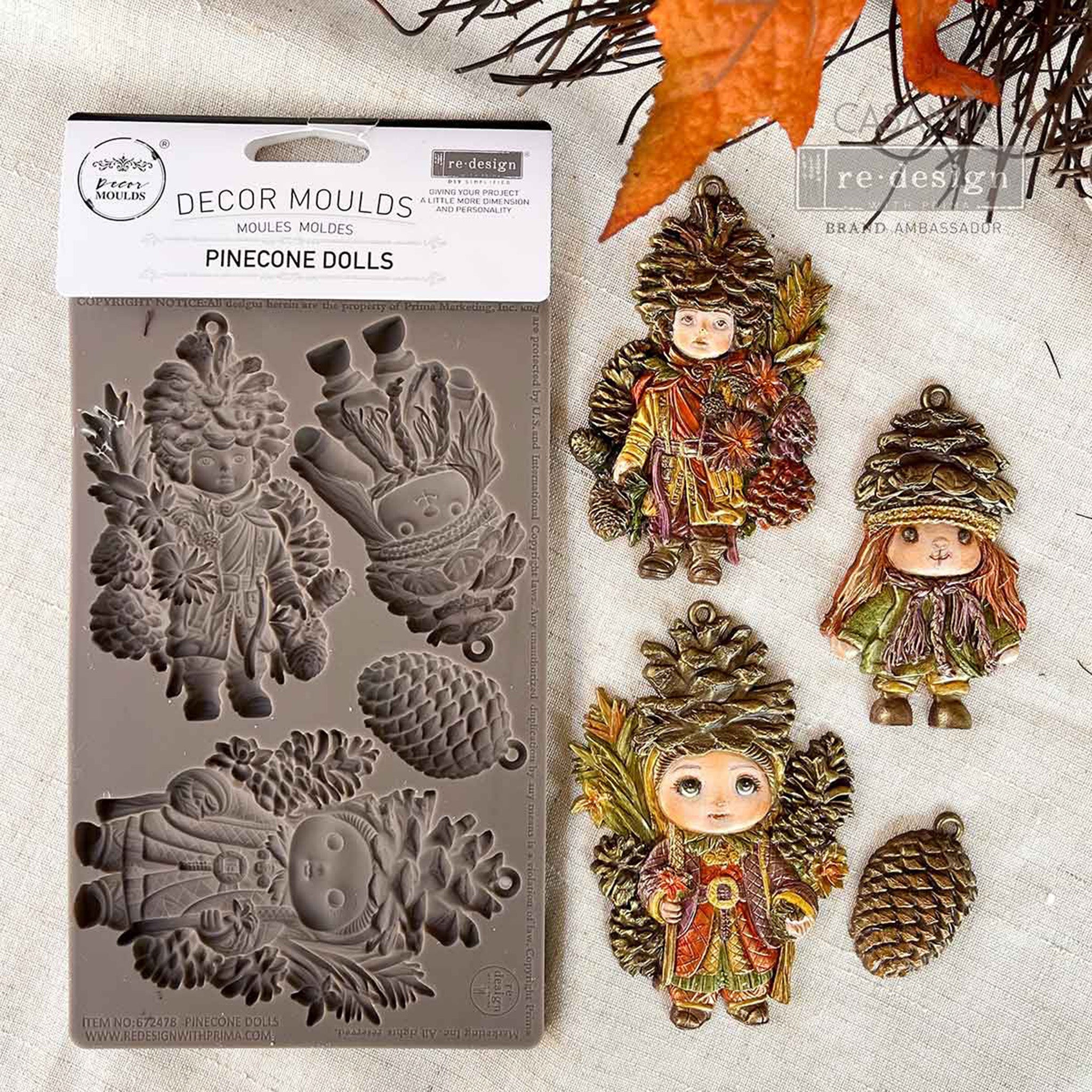 A package and colorful castings of ReDesign with Prima's Pinecone Dolls are against a white linen background.