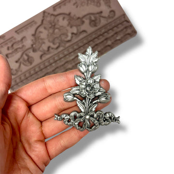 Silver floral brooch held in a hand with a decorative silicone mold in the background