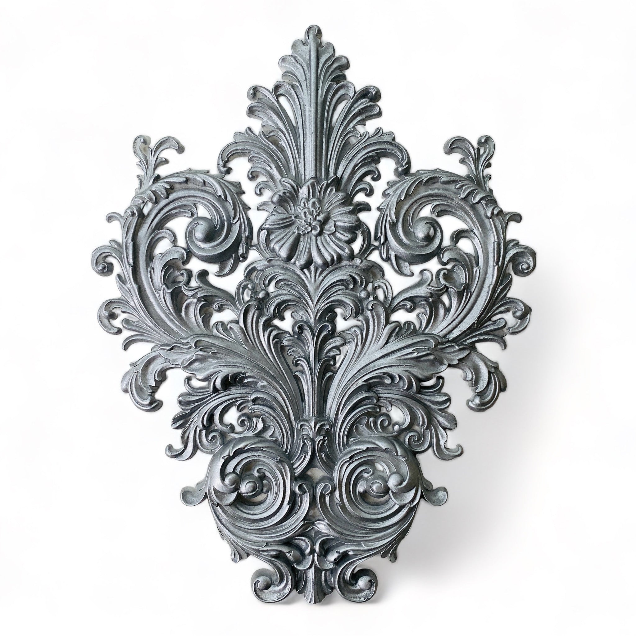 A silver-colored silicone mold casting of an ornate leaf scroll design is against a white background.